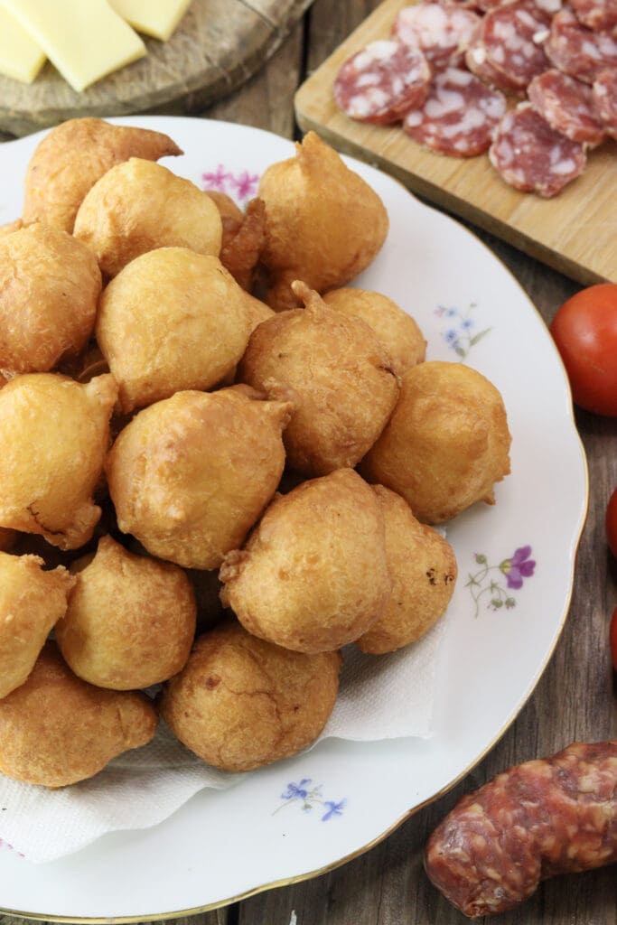 Freshly baked ustipci on a plate with salami, tomato and onions.